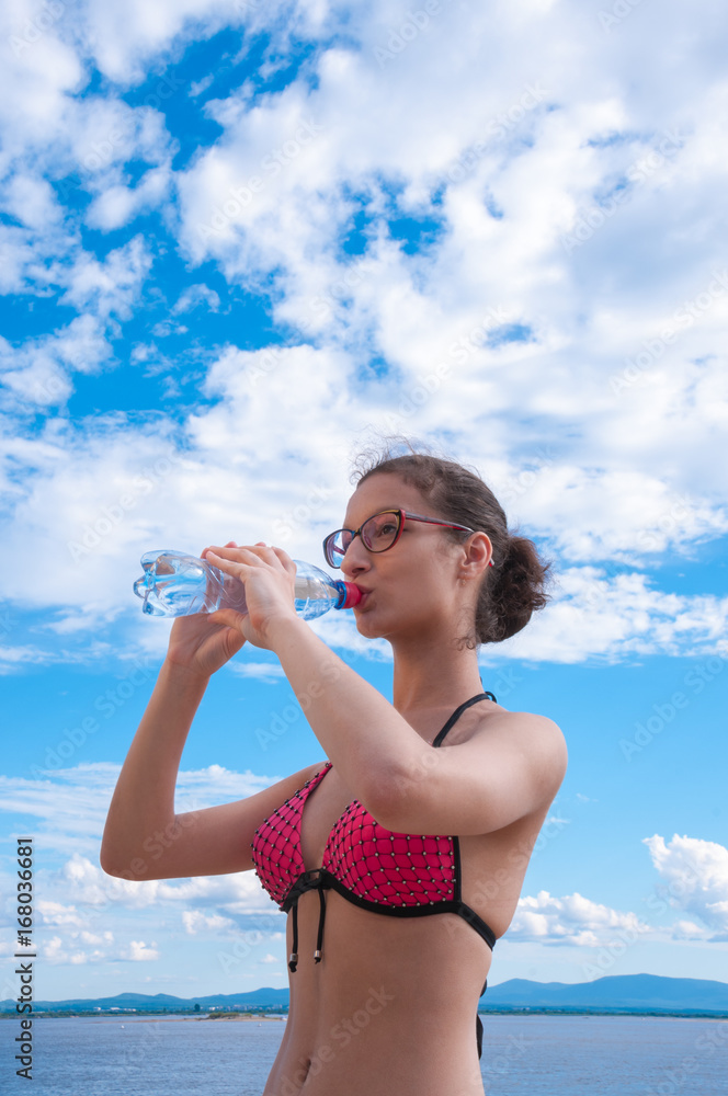 Girl wearing glasses in a bathing suit drinking water Girl wearing glasses in a bathing suit drinking water