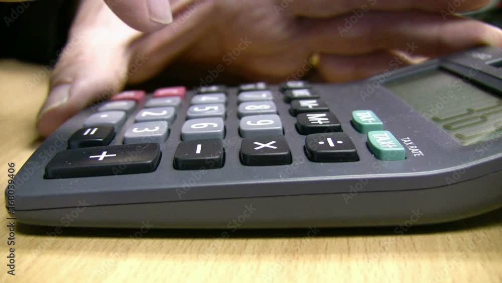 Close up side view of a desktop calculator in use, the male operator lifting the calculator to look at the total at the end. Close up side view of a desktop calculator in use, the male operator lifting the calculator to look at the total at the end.