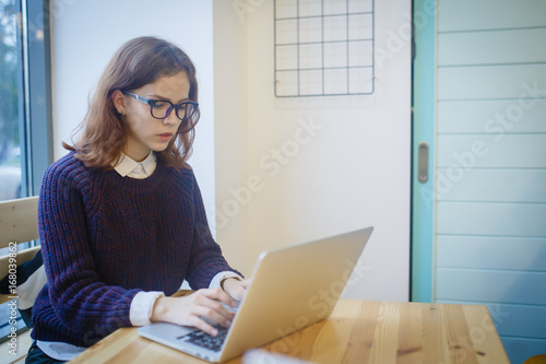 A girl sits in a cafe and prints an essay on laptop with an Internet connection