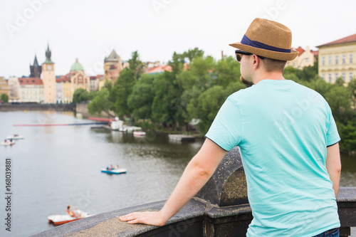 Back view of happy stylish tourist on Charles Bridge, Prague, Czech Republic. Handsome man travelling in Europe. © satura_