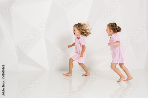 Two little funny and laughing girl in gently pink dresses playing in white studio