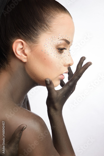 Brunette beautiful woman with crystals on face. Fashion creative black make-up on neck and hands with Swarovski.