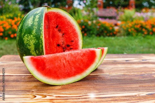 On the wooden table round sliced green striped glossy ripe watermelon with juicy red flesh on open air.