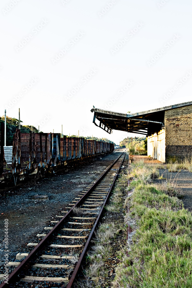 Old, rusty freight train alongside abandoned railway station.