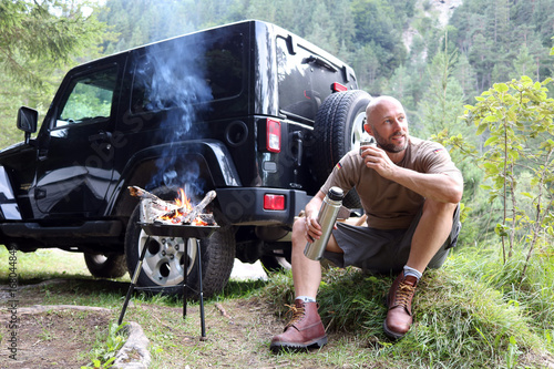 Mann grillt am Camping Platz vor SUV