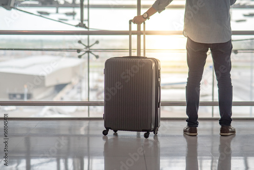 Young Asian man standing with suitcase luggage in the international airport terminal, travel lifestyle concept