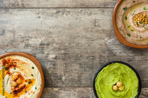 Different hummus bowls. Chickpea hummus, avocado hummus and lentils hummus on wooden table

