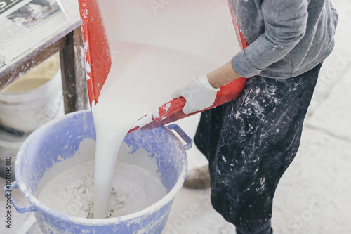 Person mixing white glazing paint in a bucket