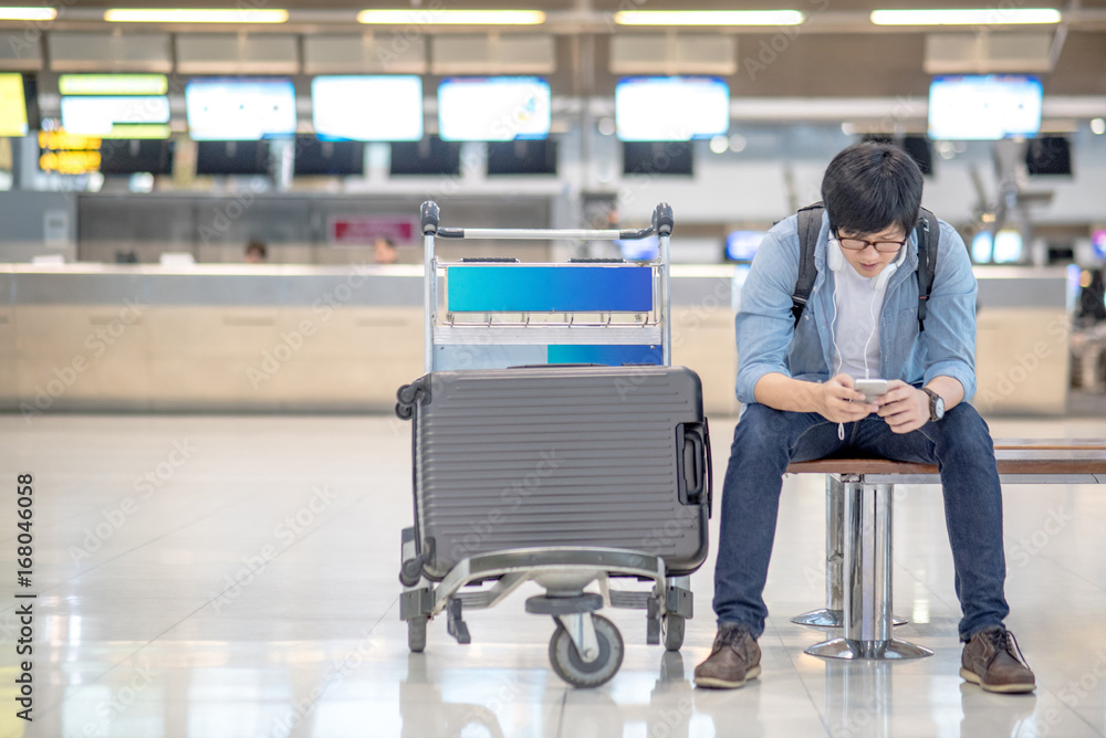 young asian guy using smartphone while waiting for check in and drop his suitcase luggage at airline check-in counter of international airport terminal young asian guy using smartphone while waiting for check in and drop his suitcase luggage at airline check-in counter of international airport terminal