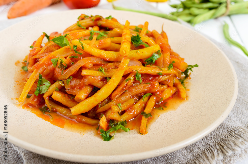 Spicy warm salad of green beans in tomato sauce on a plate on a white wooden background. Vegan dish. Spicy warm salad of green beans in tomato sauce on a plate on a white wooden background. Vegan dish.