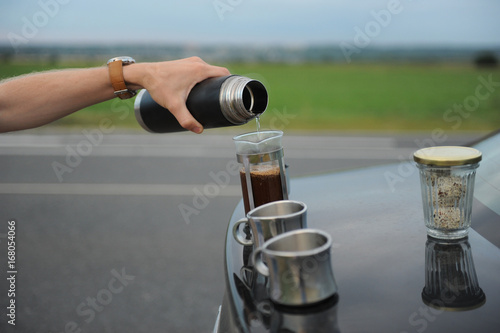 Alternative brewing coffee in a french press on the hood of a car on the side of the road on a journey