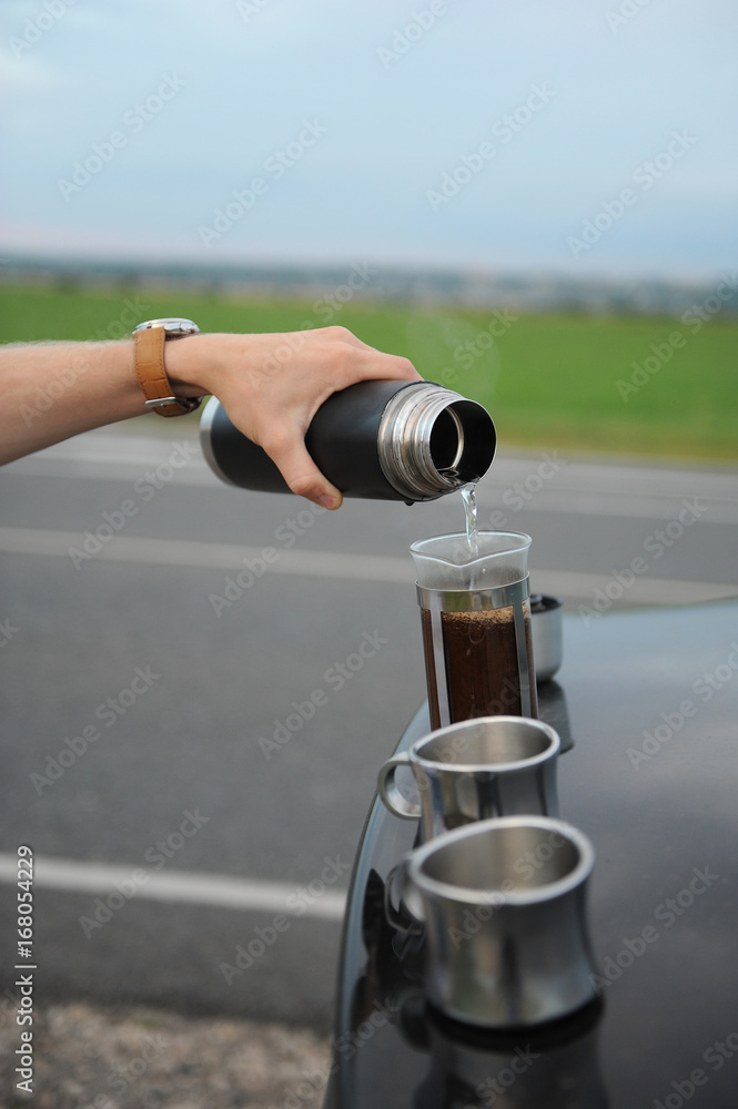 Alternative brewing coffee in a french press on the hood of a car on the side of the road on a journey
