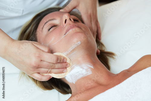 Beautiful woman with clear skin getting facial mask at salon 