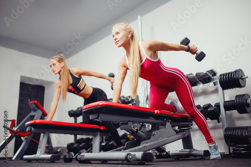 Fitness girls lift dumbbells in the gym on the bench. Concept team sports with friends.