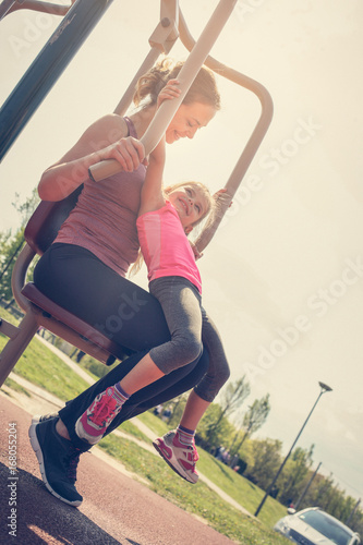 Young woman exercising outdoors. Mother and daughter in outdoor gym.