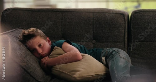 Boy laying sad on the couch holding a pillow in front of him