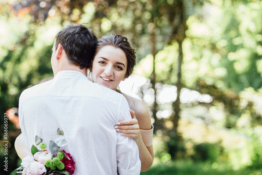 Beautiful hipster couple of happy stylish newlyweds with bouquet hugging in the sunny summer blooming park or garden on their wedding day. Beautiful hipster couple of happy stylish newlyweds with bouquet hugging in the sunny summer blooming park or garden on their wedding day.