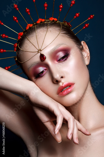 Fashion portrait of beautiful young model with professional purple makeup, perfect skin and unusual indian accessory on her head.