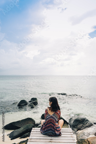 Rear view of woman sitting on the bridge and looking to sea.