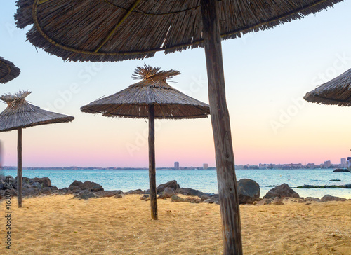 Fototapeta Naklejka Na Ścianę i Meble -  Sanset on sea with golden sand and straw-colored umbrellas.
