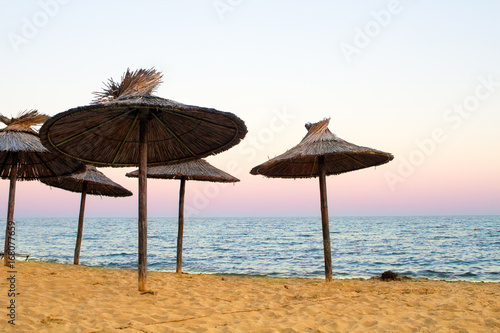 Fototapeta Naklejka Na Ścianę i Meble -  Sanset on sea with golden sand and straw-colored umbrellas.