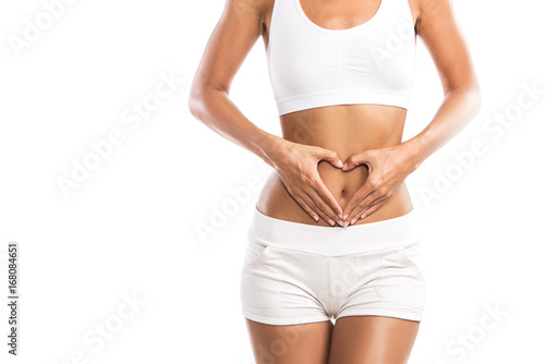Fit young woman holding a heart over her abdomen, isolated on white background