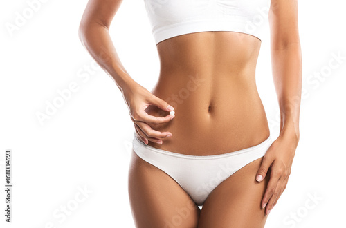 Young woman holding a pill next to her abdomen, isolated on white background, close up 