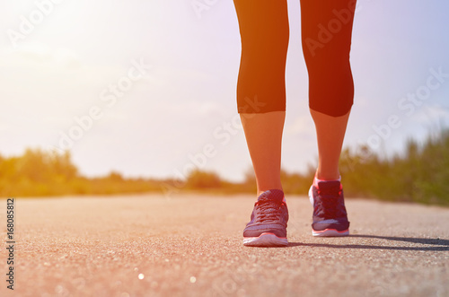 The girl runs along the road. Legs with sneakers