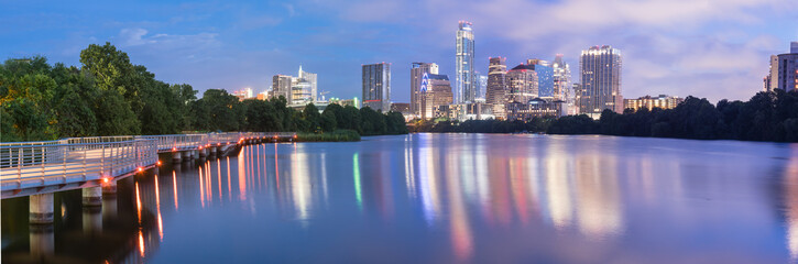 Panorama view of Downtown Austin, Texas, USA skylines reflection on the Colorado River at twilight. View from Ann and Roy Butler Hike-and-Bike Trail and boardwalk at Lady Bird Lake is on the left.