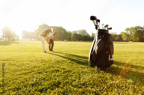 фотографія Senior male coach teaching young sportsman how to play golf