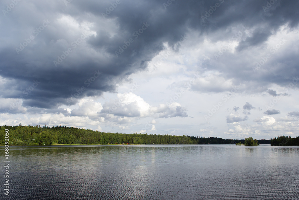 Lakeside view in Finland during summer. Stormy clouds in the sky. Green forests.