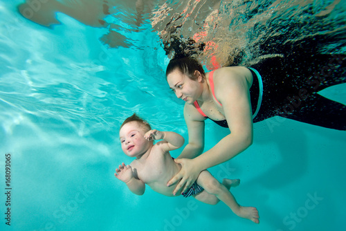 Instructor, mom teaches and helps the baby to swim underwater in the pool. Portrait. The view from under the water. Landscape orientation