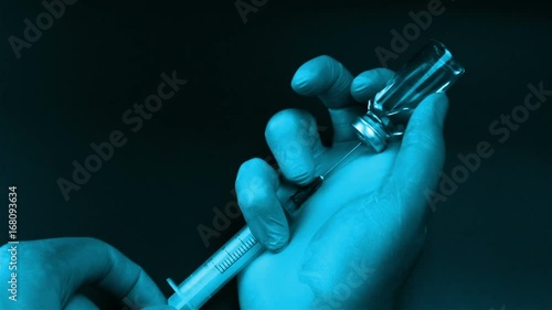 Syringe needle pierces the rubber stopper of the glass vial and filling syringe from glass ampule on black background