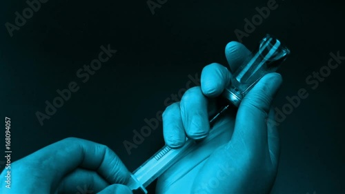 Syringe needle pierces the rubber stopper of the glass vial and filling syringe from glass ampule on black background
