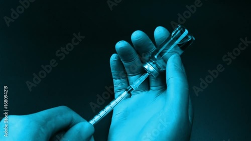 Syringe needle pierces the rubber stopper of the glass vial and filling syringe from glass ampule on black background