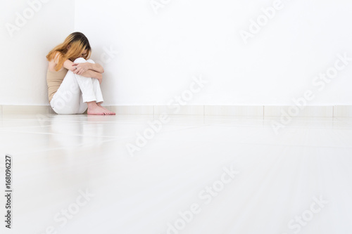Depressed woman sitting in the corner of the room. The walls are white and the room is empty.. photo