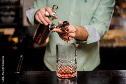 Bartender making alcoholic cocktail , metal jigger and bar environment
