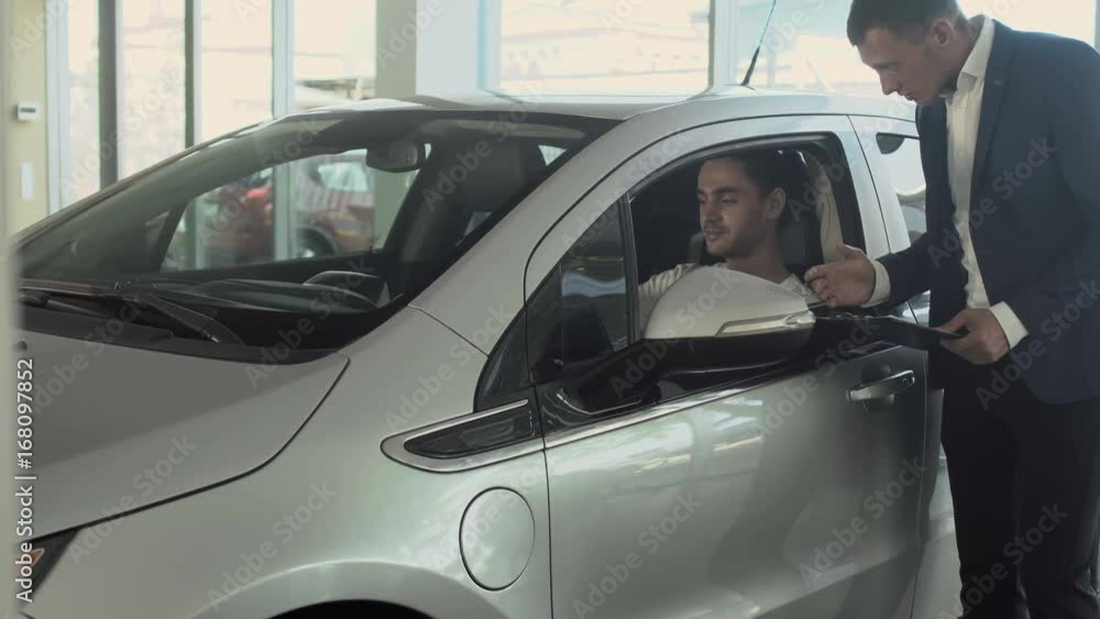 Stylish man talks with salesman and inspects the car's cabin in car dealership Stylish man talks with salesman and inspects the car's cabin in car dealership