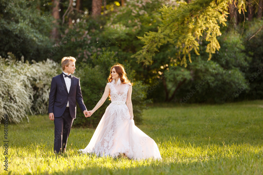 Young Bride and Groom couple in a blooming garden. Tender holding each other. Spring wedding. Redhead girl with long hairs. Young family outdoor image near blooming bush of spirea. Love and tenderness Young Bride and Groom couple in a blooming garden. Tender holding each other. Spring wedding. Redhead girl with long hairs. Young family outdoor image near blooming bush of spirea. Love and tenderness