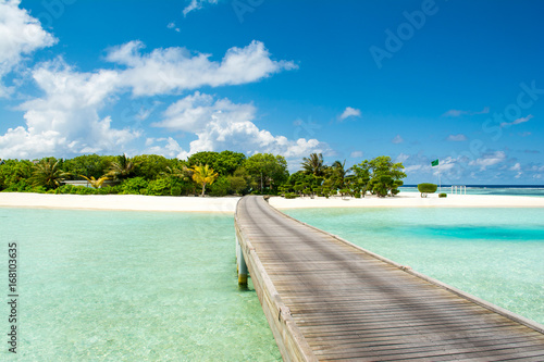 Wooden bridge to beautiful sandy beach under the shade of palms and tropical plants, Maldives