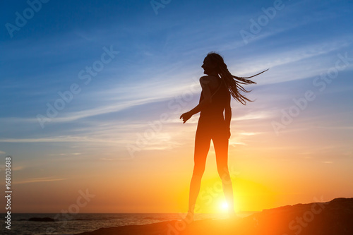 Silhouette of flexible dancing girl on the sea coast during a sunset.