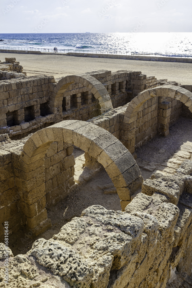 Ancient roman bathhouse ruins in Caesarea harbor national park with blue sea and promenade