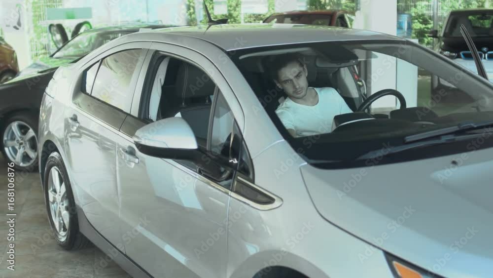 The guy inspects the car from inside before the purchase it in car dealership The guy inspects the car from inside before the purchase it in car dealership