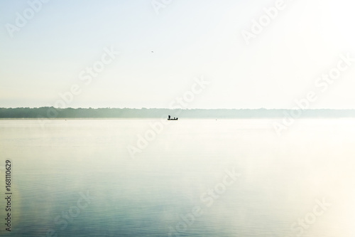 Glassy calm, misty morning lake and fishing boat