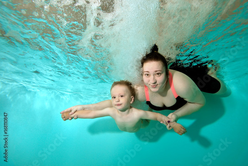 Mom with little son swimming underwater in the pool, spread his arms and looking at me. Portrait. Shooting under the water surface. Landscape orientation