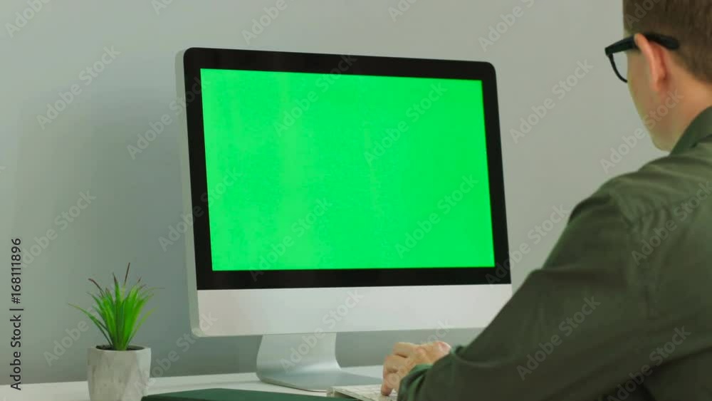 Close up shot of young man in the glasses using computer with green screen at the modern office table. Chroma key. Close up shot of young man in the glasses using computer with green screen at the modern office table. Chroma key.