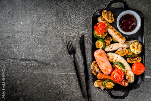 Barbecue. Assortment of various grilled meat sausages, with vegetables BBQ - mushrooms, tomatoes, zucchini, onions. On a black stone table, on a black plate, with sauce. Copy space top view