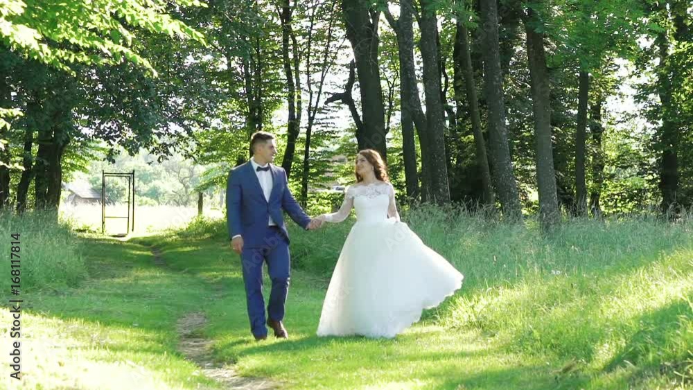 Smiling bride posing at her handsome groom, walking and kissing. Slowly