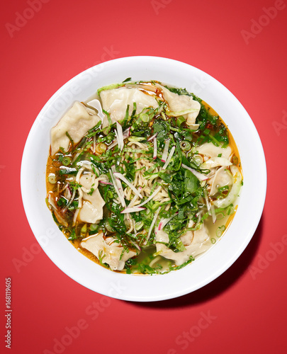 asian dumplings with broth in white bowl, on red background, studio