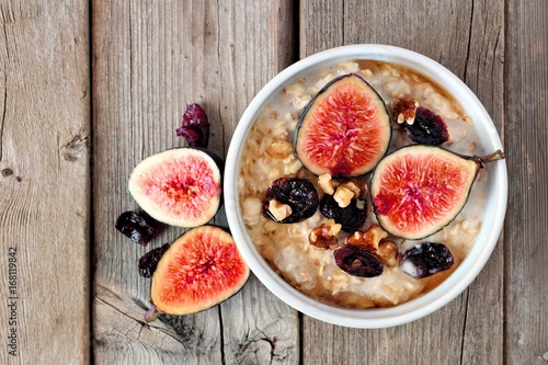 Oatmeal with red figs, cranberries and walnuts in a bowl, above view on rustic wood